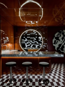 Modern bar counter featuring black and white tiles, metallic ceiling, and stools.