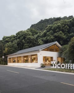 Modern white exterior of a coffee shop with large windows and a wooden roof.