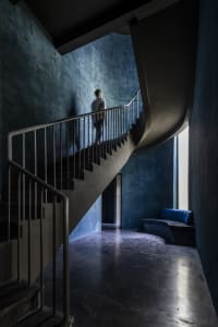 A modern, industrial-style staircase with concrete treads and metal railings, illuminated by natural light from a high window