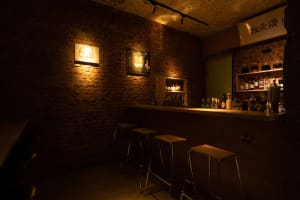 A dimly lit restaurant bar with brick walls, industrial lighting, and a wooden counter.