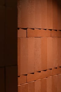 A textured brown brick wall with sunlight casting shadows on the surface.