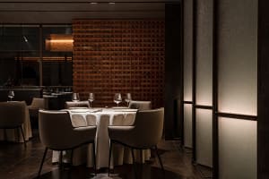 A dimly lit dining room with a brick wall, round table set for four, and sleek, modern chairs.