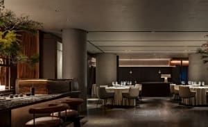 A spacious, contemporary bar interior featuring modern furniture, concrete elements, and warm lighting.