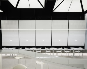 A minimalist cafe interior with white tables and chairs, white beadboard walls, and a sleek white countertop.