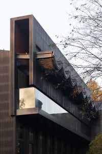 A modern building exterior clad with dark metal material, featuring geometric shapes and large glass windows.