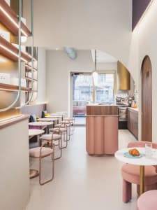 Pastel-colored cafe interior with round tables, chairs, and bar area.