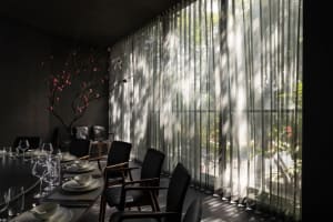 A modern restaurant dining area with sheer curtains, glass walls, and minimalist black chairs.