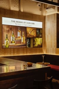 Modern wine bar interior with wooden accents and a large display of Suntory whiskey bottles.