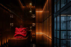 A dark corridor featuring a striking red lion head statue and wooden tiles with traditional Chinese characters.