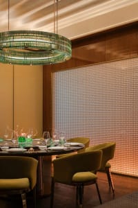 An industrial-style restaurant interior with black marble table, green glass chandelier, and green upholstered chairs.