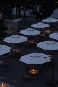 Outdoor seating arrangement of wooden tables and chairs under white umbrellas with candle lights.