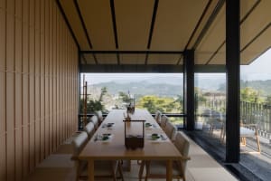 Minimalist dining room with wooden furniture and a view of mountains through large windows.
