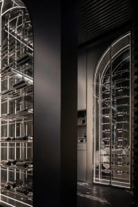 A modern wine cellar with glass and metal storage racks filled with wine bottles.