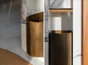 A metallic trash bin made of bronze standing next to a marble column in an interior setting.