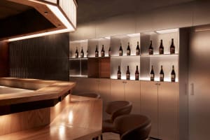 A modern bar interior featuring wooden fixtures, metal shelves, and glass bottles.
