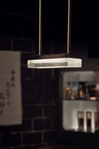 Modern industrial pendant light fixture with frosted glass diffuser hanging from steel cords in a restaurant setting.