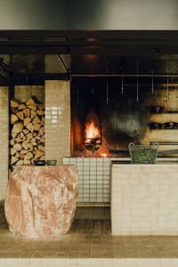 An industrial-style commercial kitchen with exposed brick walls and a firewood-stocked fireplace.
