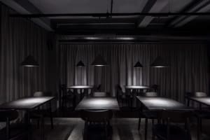 An empty minimalist-style restaurant interior with metal pendant lights and wooden tables.