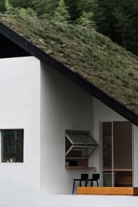 Modern minimalist white stucco house with a green grass-covered roof and contemporary black furniture on the porch.