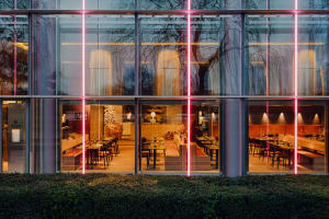 Contemporary restaurant with glass walls and wooden seating, illuminated by red neon lights.