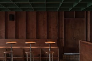 A minimalist bar area with a modern design featuring wooden and metallic surfaces and industrial stools.