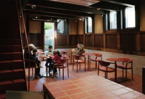 People sitting at dining tables in a rustic restaurant with wood paneling and red table legs and seats.