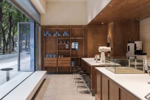 Modern coffee shop with wooden counter, glass shelves, and metal stools.