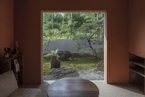 A serene modern interior featuring a gardenscape through a large window with stone, glass, and wooden elements.