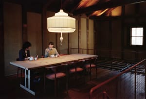 Two people sitting at a wooden table with traditional Japanese interior design elements, including a large hanging lantern.