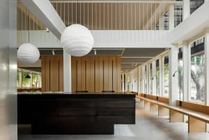 A modern coffee shop interior with wood and concrete materials, featuring a dining counter and ample seating.