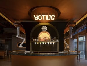 A modern bar area with curved metal and glass fixtures, featuring a circular sign with the word 'YOTING' and a bar counter wi