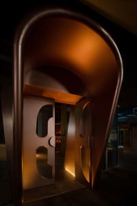 A modern entryway featuring matte metallic arches framed in glass with warm lighting.
