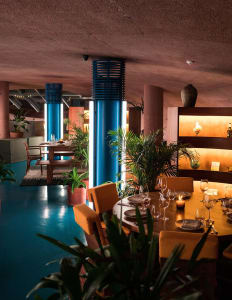A modern restaurant interior with metallic columns, indoor greenery, and round tables.