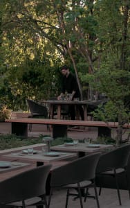A modern restaurant terrace with wooden furniture and greenery surrounding the dining area.