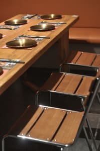 A modern restaurant interior featuring wooden benches and metal-frame chairs, placed at a wooden dining table.