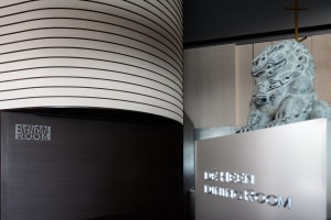 A stylized entryway with metal cladding and concrete walls featuring the signage for De Heen Dining Room.