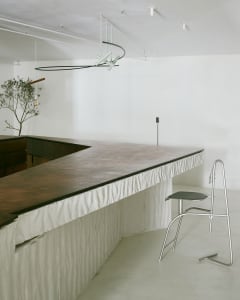 A minimalist modern bar with a concrete countertop and a single metal chair.