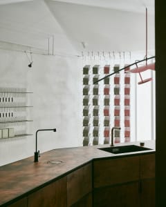 A modern kitchen with a metallic countertop, industrial style lighting, and a row of suspended shelves.