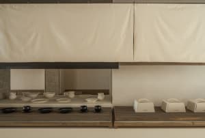 A modern coffee shop display featuring wooden shelves with white ceramic dishes and black coffee cups.