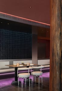 Modern restaurant interior with black tiles, metallic furniture, and purple lighting