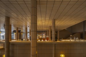A modern retail bar with tiled walls and floors, featuring a bar counter with various drinks.