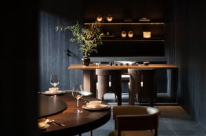 Modern restaurant interior with wooden tables, chairs, and dark, minimalist decor.