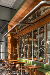 A modern cafe interior featuring wooden tables, glass windows, and green accents.