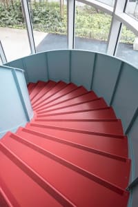 A spiral red staircase made of metal, leading downwards.
