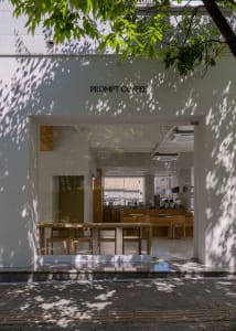 A minimalist coffee shop with glass and wooden features, seen from the exterior.