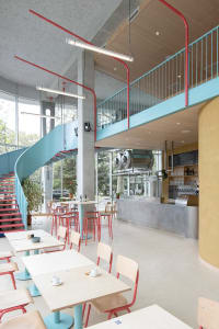 A modern cafe with a concrete staircase and colorful seating areas.