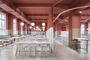 Large modern cafeteria with white tables and chairs, red painted concrete walls, and hanging spherical lights.