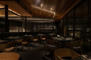 A modern restaurant interior designed with wooden elements, featuring round tables set for dining and a cozy atmosphere.
