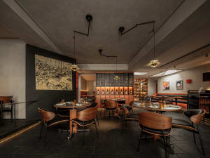 A modern restaurant interior featuring plush chairs with woven fabric upholstery, round tables with elegant tableware, and a 