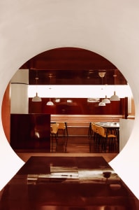 A modern restaurant interior with red metallic walls and white pendant lights.
